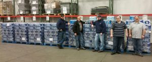 Charter Communications employees pose next to more than eight pallets of drinking water gathered for Flint residents at Charter Michigan offices