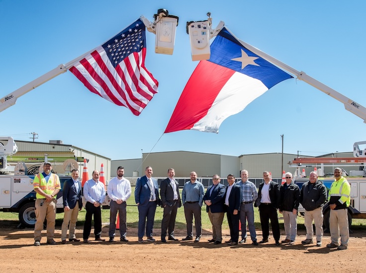 Spectrum officials pose under the American flag and State of Texas flag hanging from two bucket truck buckets