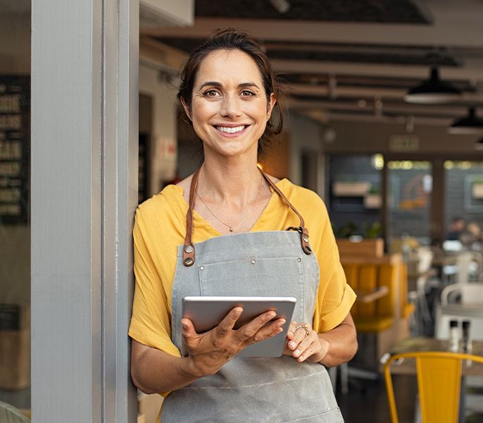 Woman holding a tablet smiling in the doorway of her small business
