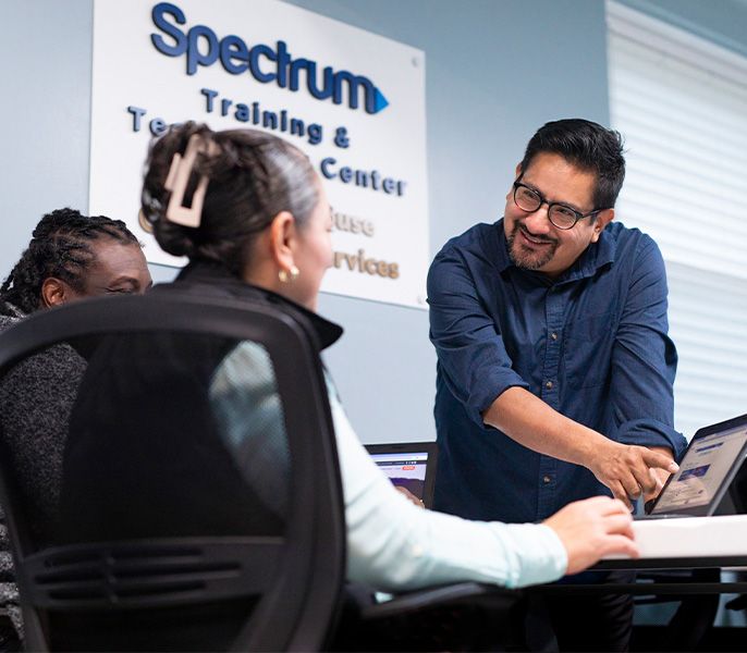 An instructor teaching two adult students in a computer lab