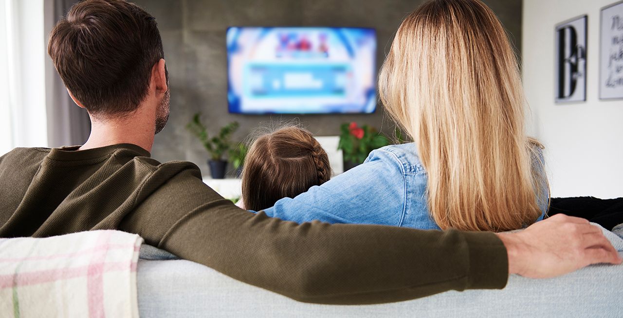 Family watching TV programming from their living room couch, viewed from behind