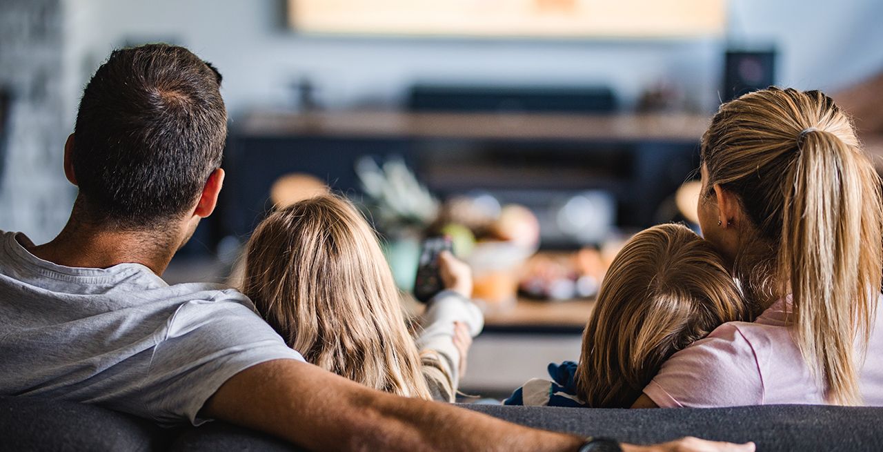 Family watching TV programming from their living room couch, viewed from behind