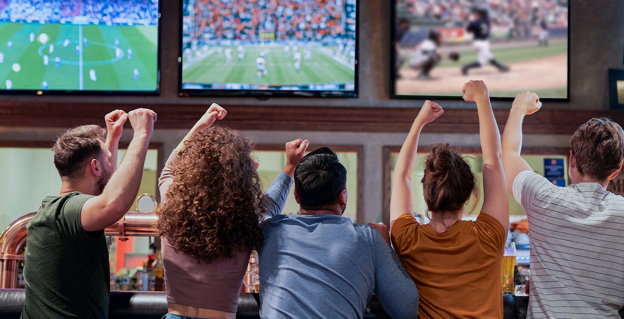 A bar scene with patrons cheering at sports programming on TVs