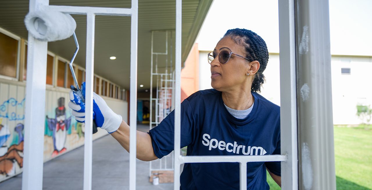 Female Spectrum volunteer painting a railing white at a community center
