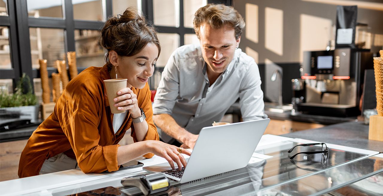 Man and woman business owners looking at a laptop together in their place of business smiling