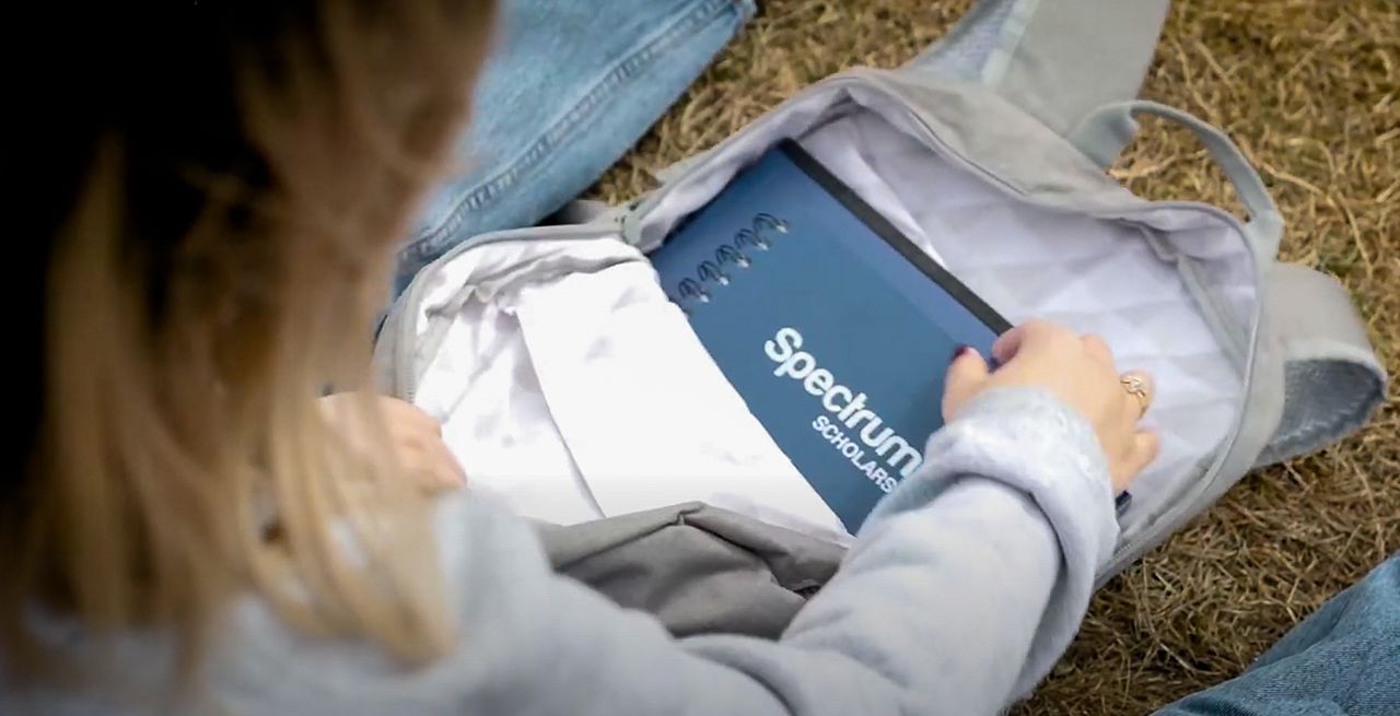 Spectrum Scholar looks into her Spectrum branded backpack on a college campus