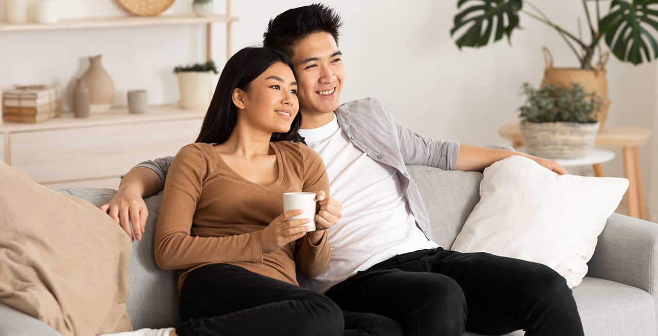 Asian American couple watching TV from their couch in their living room, smiling