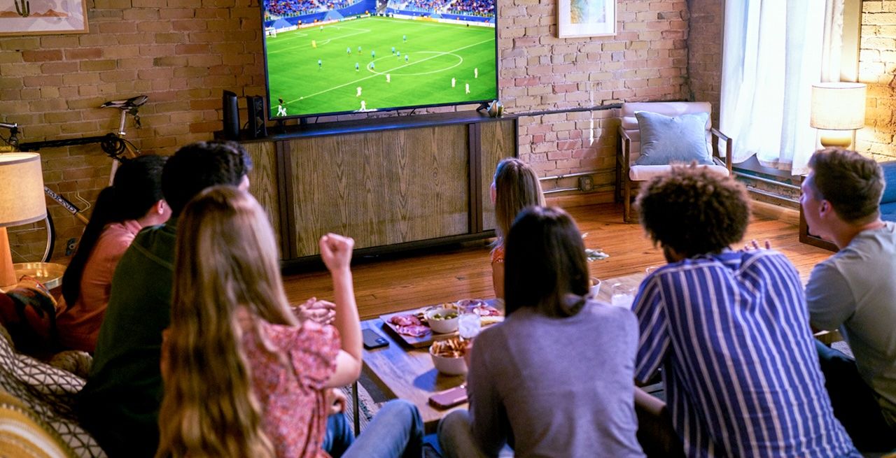 Family watching soccer game on their TV in their living room, viewed from behind