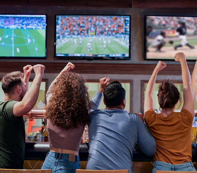 Sports fans cheering at sports programming on TVs at a crowded bar