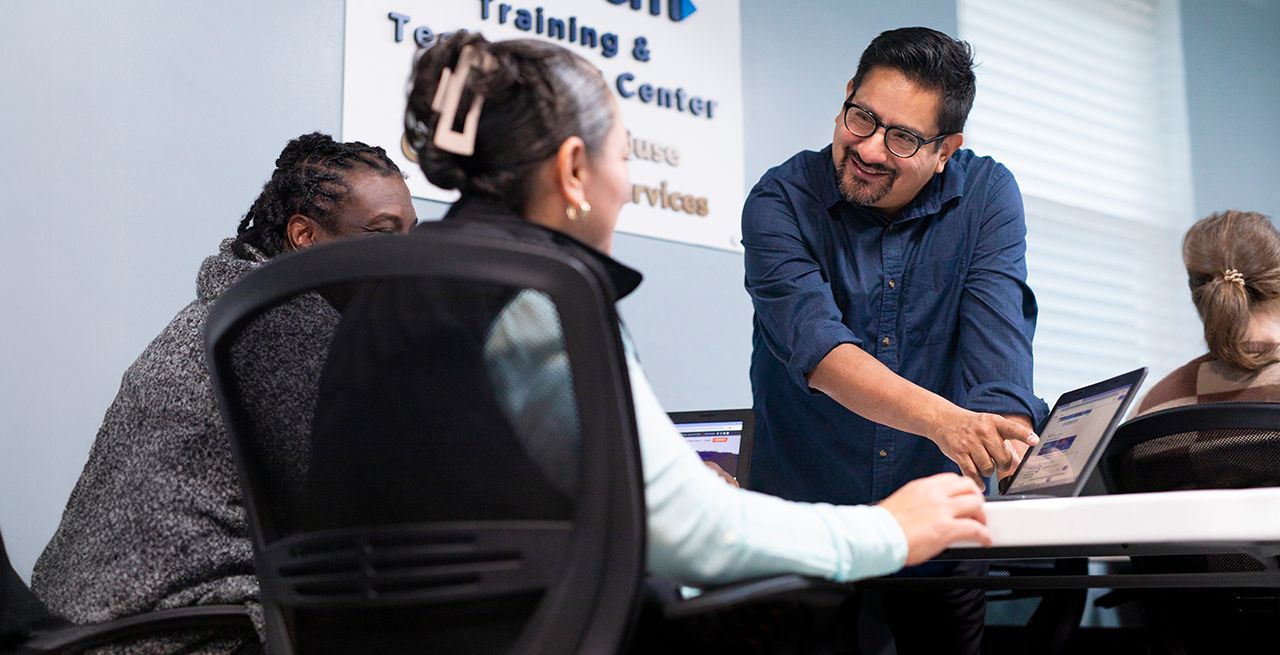 An instructor teaching two adult students in a computer lab