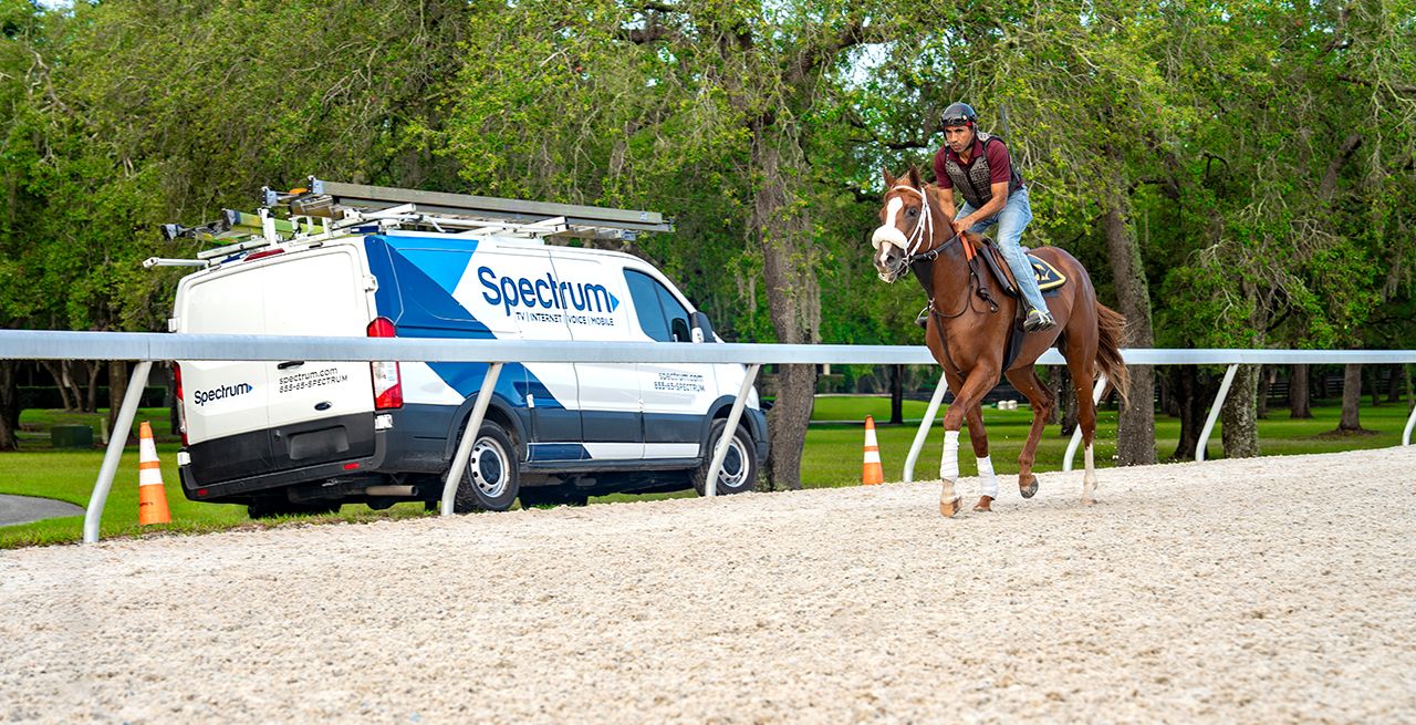 A horse gallops on a track at GoldMark Farm in Ocala, Florida, with Spectrum Van in background