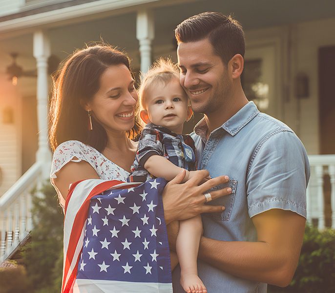 Image of a family with a baby in front of a porch with an American flag