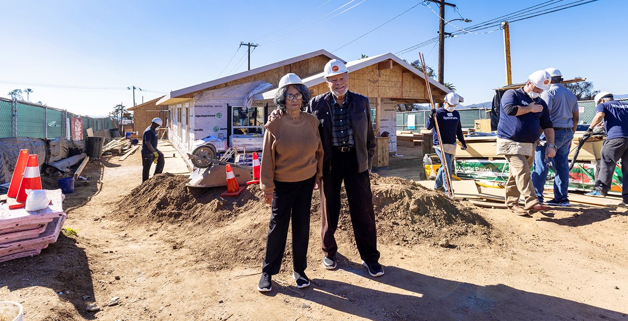 A couple watches their house being rebuilt by Spectrum volunteers