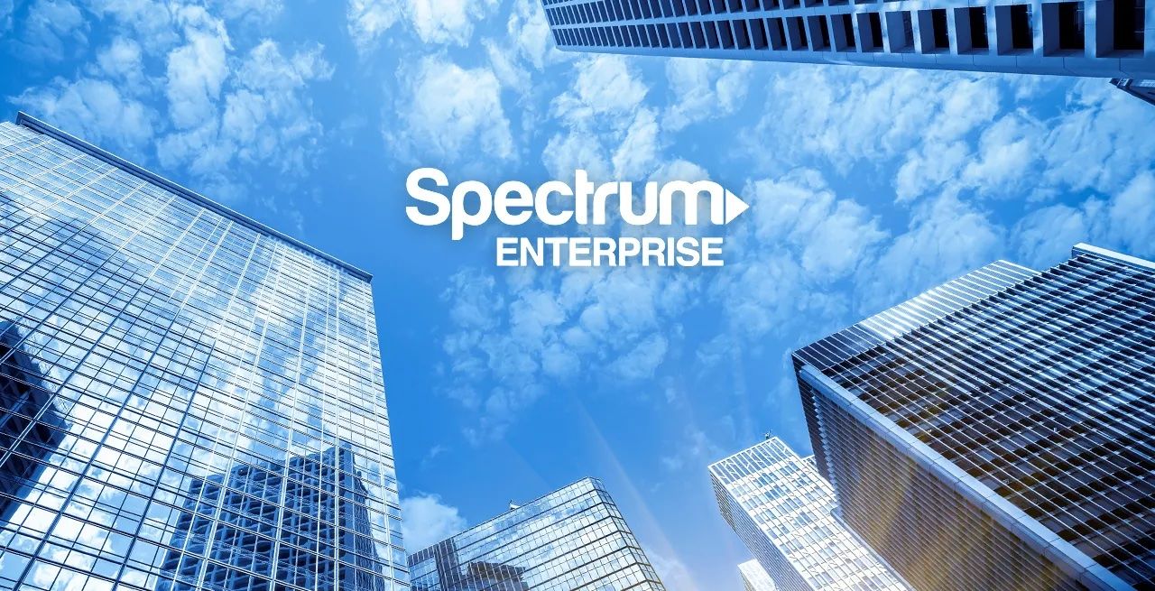 View of tall office buildings from the ground with Spectrum Enterprise logo on a blue sky