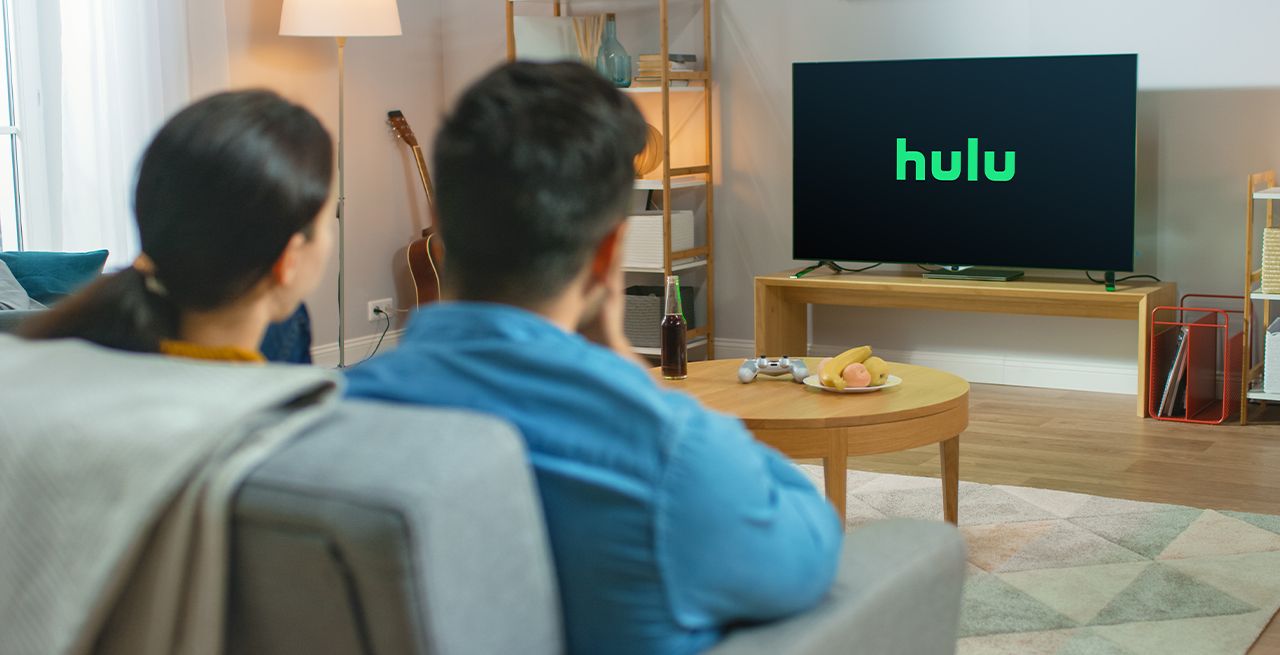 Family watching TV programming from their living room couch, viewed from behind