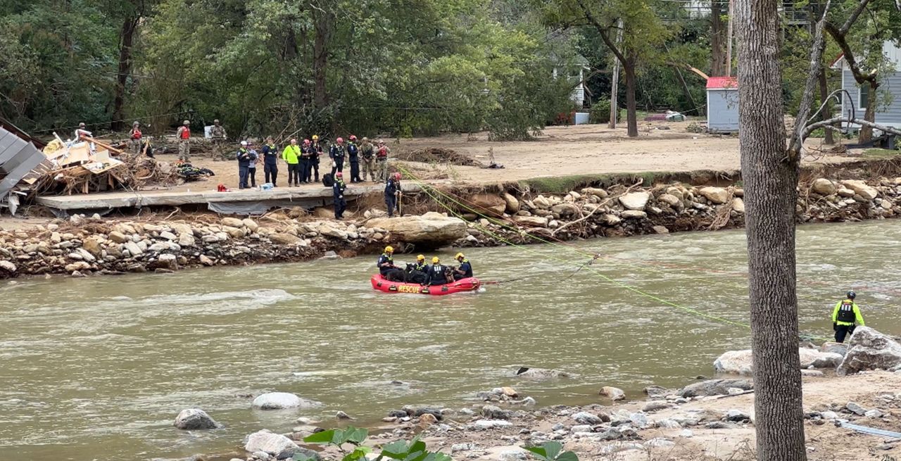 Rescuers in a life raft on a raging river, with other emergency personnel on shore looking on