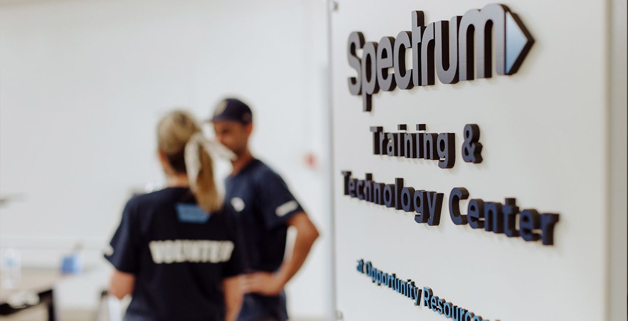 Spectrum Technology and Training Center signage on a wall with volunteers blurred in the background