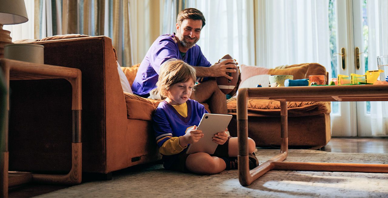 A father and son in their living room, the son using a tablet