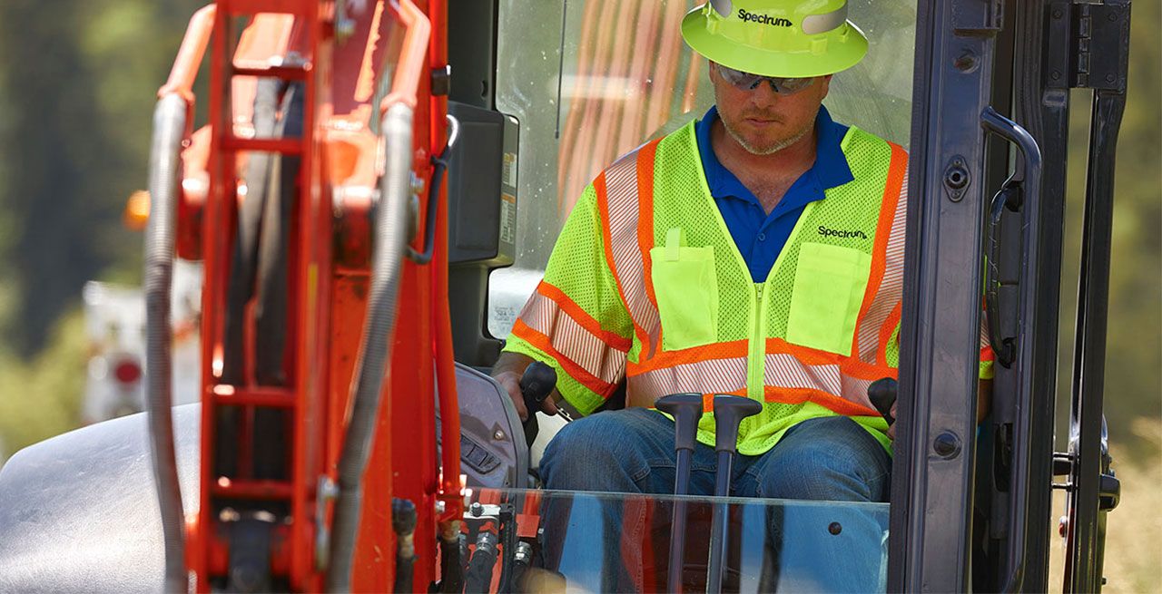 Spectrum technician using a backhoe to bury conduit