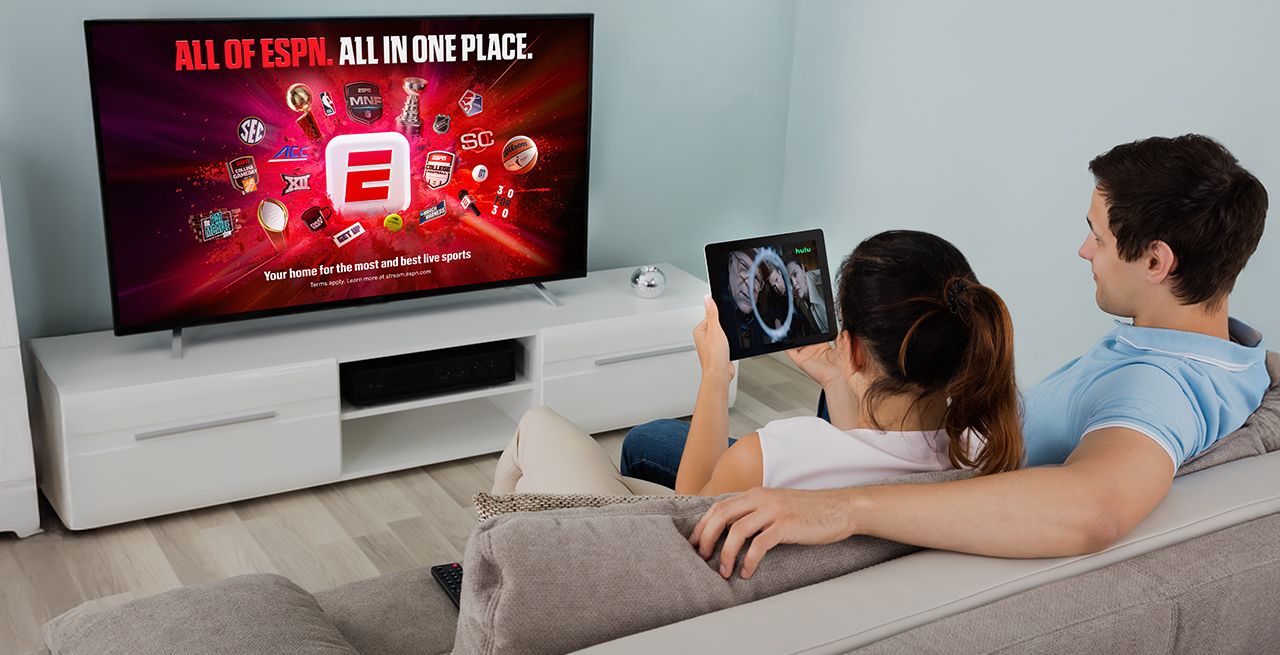 A man and woman watching ESPN and Hulu content on their devices