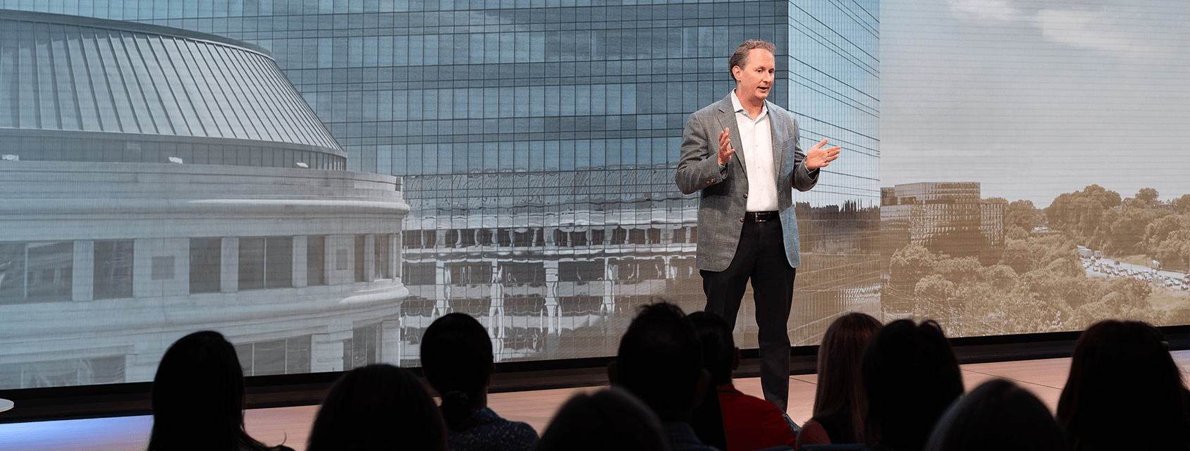 Chris Winfrey speaking on stage to a group of people with a building background