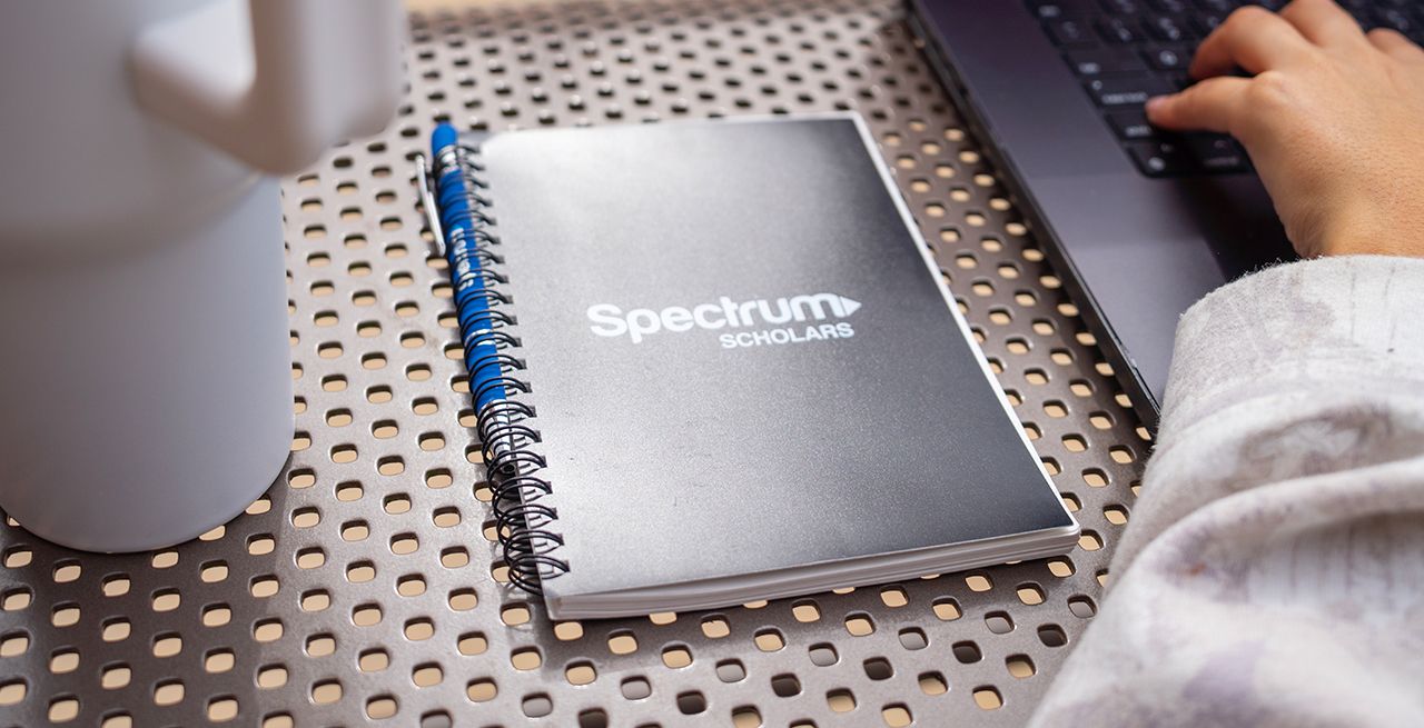 A Spectrum Scholars branded notebook sitting next to a laptop on a table