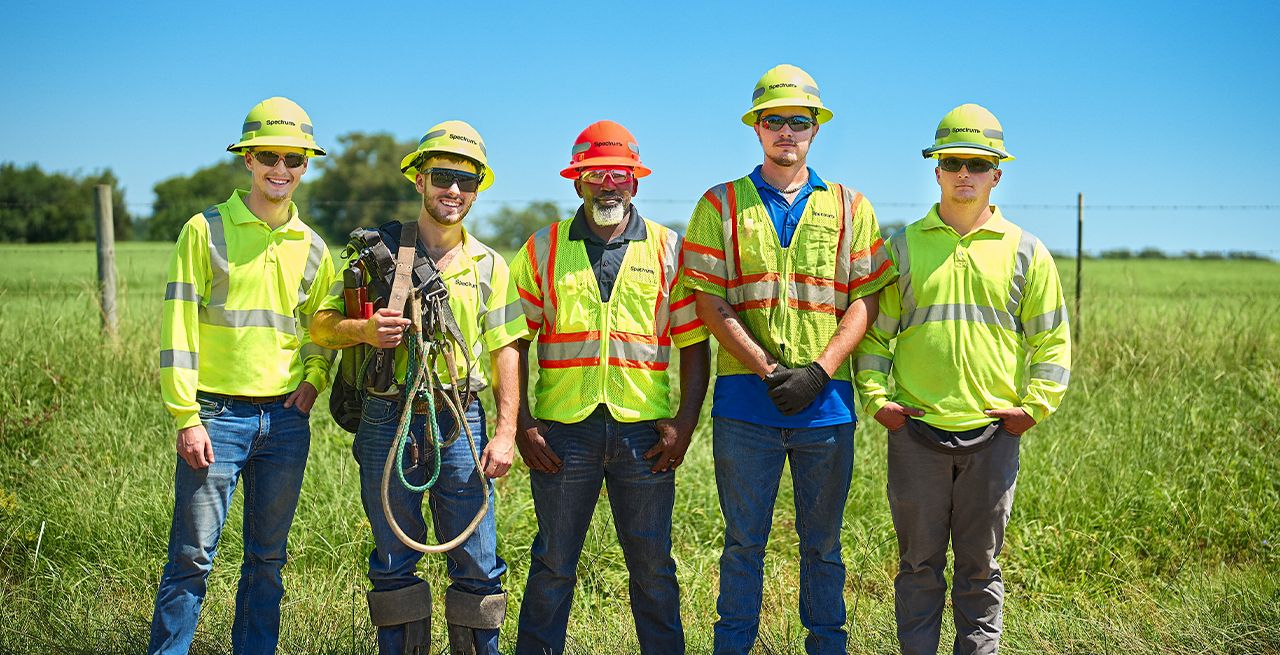 A group of five Spectrum field technicians posing in a row in a rural location
