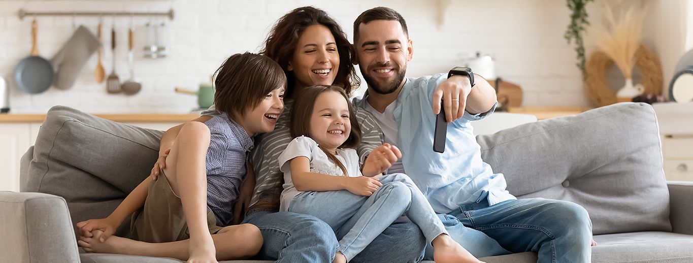 A happy family of four using their devices on their living room couch