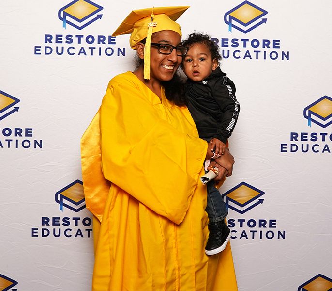 Miquella poses with her child at her graduation - she was referred to Restore Education, a nonprofit that partners with Charter’s Spectrum Community Center Assist program, which changed her life.