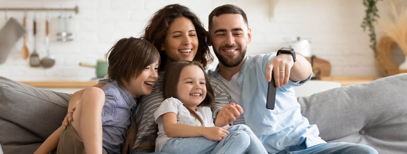 A happy family of four using their devices on their living room couch