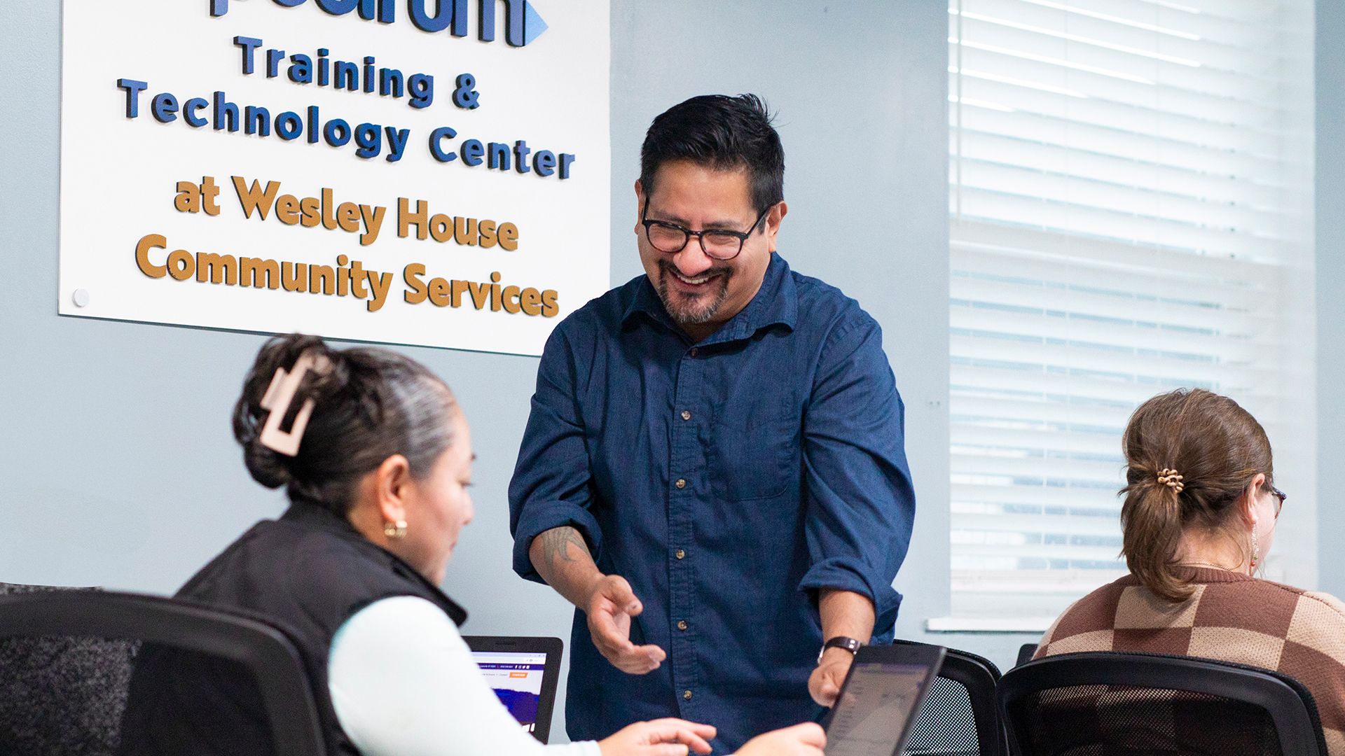 An instructor teaching two adult students in a computer lab