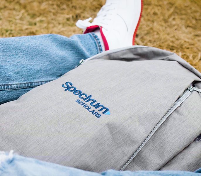 Backpack with Spectrum logo on the ground next to college student's legs